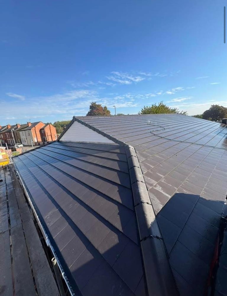 Solar panel installation on residential roof with blue sky and neighboring brick buildings visible in background
