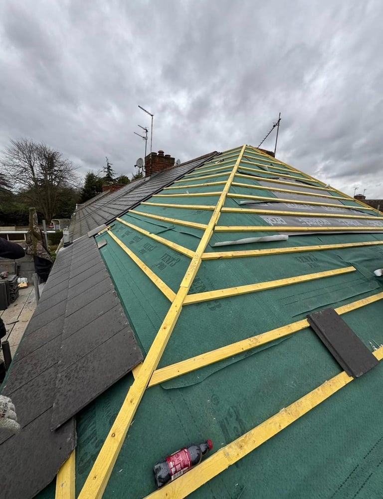 Roof under renovation with yellow wooden beams on green protective sheeting against cloudy sky