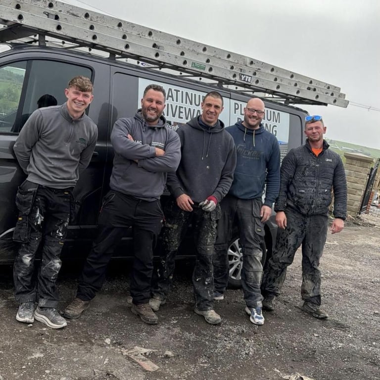 Five workers in muddy work clothes stand together in front of a black van on a rural construction site