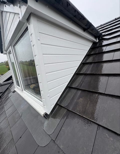 White dormer window with horizontal vents on wet dark roof shingles of a residential home