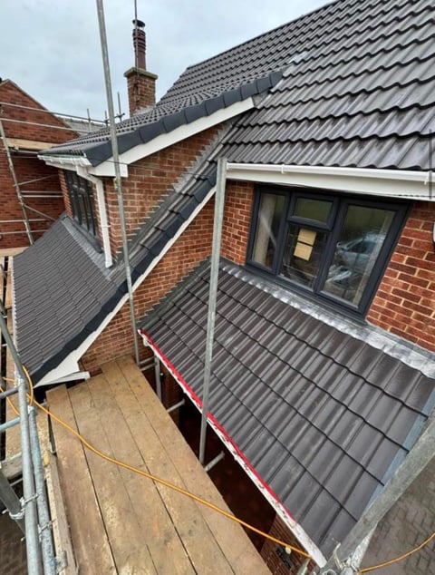 New metal roof with guttering installed on brick house during construction with scaffolding surrounding the building